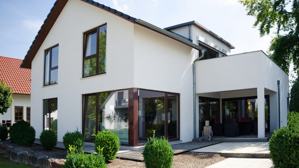 Freistehendes Wohnhaus mit hellem Putz, Satteldach, bodentiefen Fenstern und angebautem Flachdach-Anbau